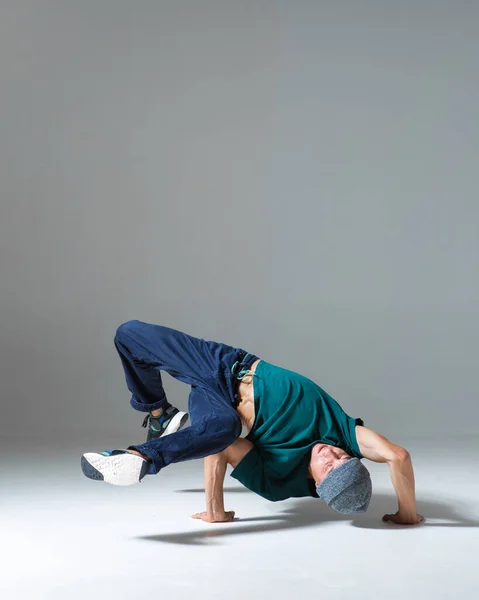 Stylowy młody facet breakdancer tańczy hip hop na podłodze w studio odizolowany na szarym tle. Plakat szkoły tańca — Zdjęcie stockowe