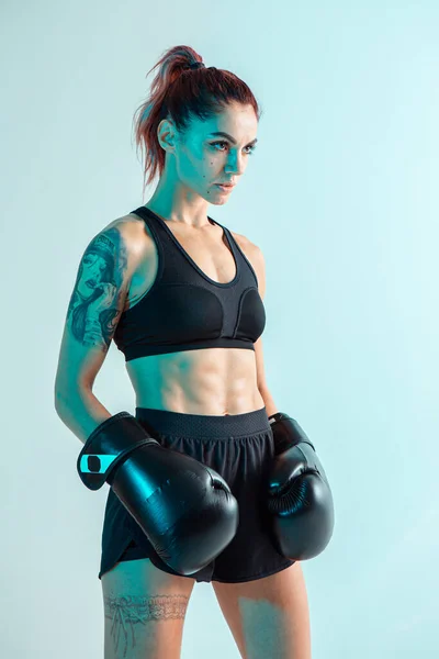 Boks eldivenli atletik kız boksör stüdyoda mavi ışıkta poz veriyor. Karışık dövüş sanatları posteri. Dövmeli vücut. — Stok fotoğraf