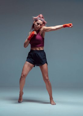 Stüdyoda gri arka planda izole edilmiş havalı kadın boksör. Karışık dövüş sanatları posteri