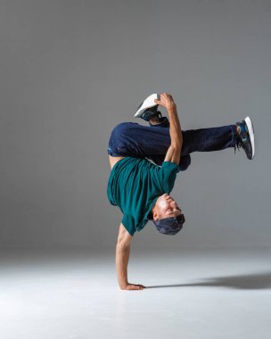 Gri arka planda tek başına duran havalı break dansçı adam dans ediyor. Breakdance dersleri