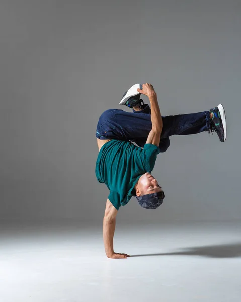 Menő srác breakdance táncos a padlón álló egyik kezén elszigetelt szürke háttér. Breakdance órák — Stock Fotó