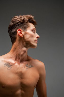 Stüdyoda şık saç kesimi ve çıplak omuzları olan yakışıklı bir adam portresi gri arka planda izole edilmiş.