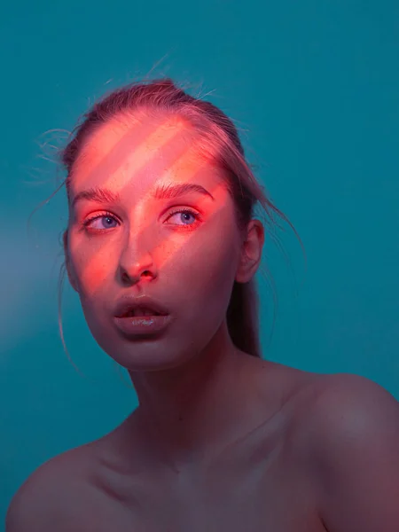 Trendy portrét mladé hezké dívky s korálovým světlem vzor z žaluzií na její tváři izolované na modrém pozadí studia — Stock fotografie