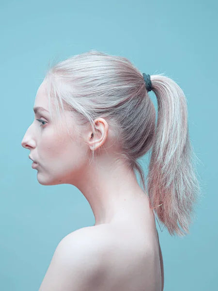 Profiel van jong blond meisje met paardenstaart op blauwe achtergrond in studio. Reclameposter voor cosmetica — Stockfoto