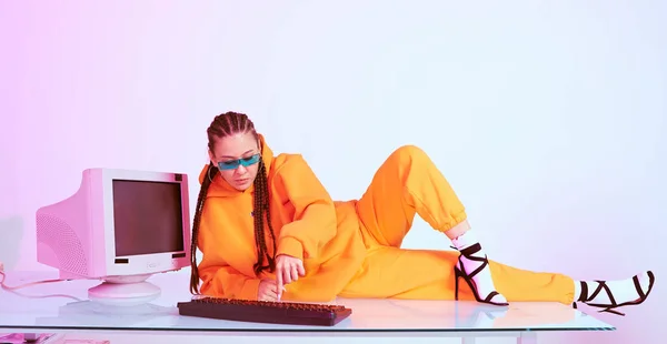 Elegante mujer asiática trabajadora de oficina en gafas de sol colocadas en la mesa con computadora obsoleta escribiendo en luz de neón — Foto de Stock