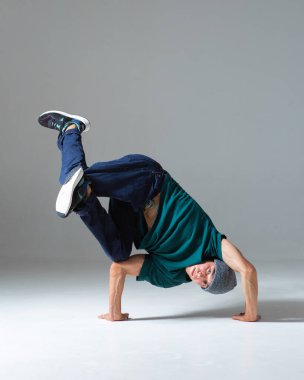 Şapkalı şık genç break dansçı gri arka planda tek başına el ele dans ediyor. Dans okulu posteri