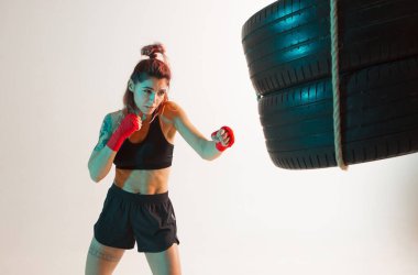 Neon Stüdyo ışığı altında lastiklerden yapılmış kum torbasıyla atletik kız eğitimi. Kadınların spor posteri.
