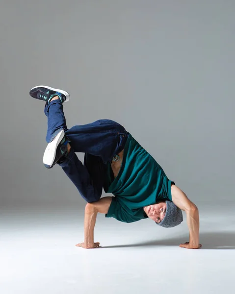 Stylowy młody facet breakdancer w kapeluszu stoi na rękach taniec hip hop odizolowany na szarym tle. Plakat szkoły tańca — Zdjęcie stockowe