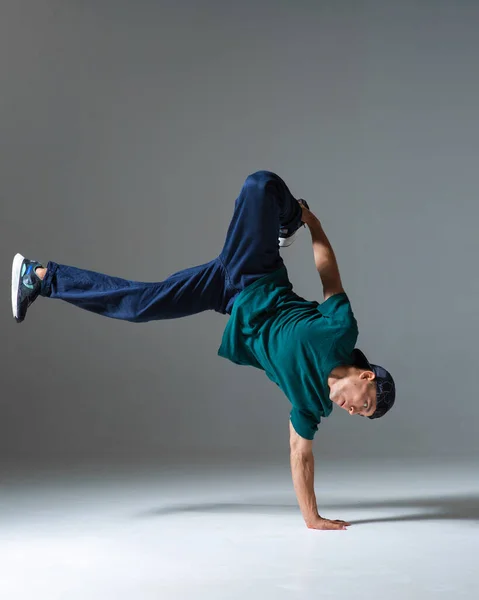 Fajny facet breakdancer taniec na podłodze stojąc na jednej ręce odizolowany na szarym tle. Lekcje przerwy — Zdjęcie stockowe