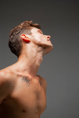 Stüdyoda tişörtsüz, şık saç kesimi olan yakışıklı bir gencin portresi. Dövmeli vücut.