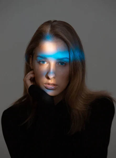 Tvůrčí portrét stylové mladé ženy s modrým neonovým světlem na obličeji a dokonalou pletí na šedém pozadí — Stock fotografie