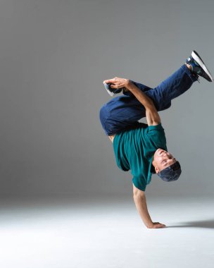 Gri arka planda tek başına duran havalı break dansçı adam dans ediyor. Breakdance dersleri