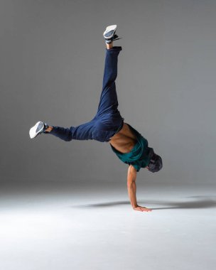 Havalı break dansçı bir elinde gri arka planda izole bir şekilde yerde dans ediyor. Breakdance dersleri