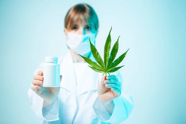 Médecin féminin avec un bocal blanc maquillé et une feuille de chanvre dans les mains en lumière bleu néon studio. Compléments alimentaires biologiques — Photo