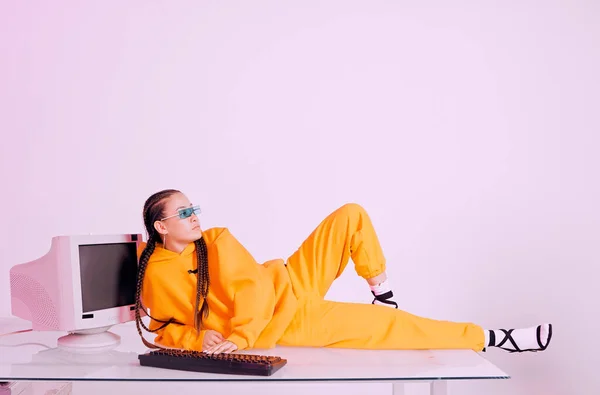 Cool asian female office worker in sunglasses laying on table with obsolete computer. Colored light