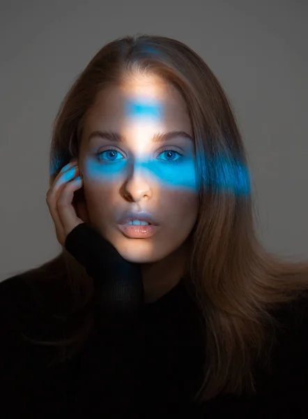 Porträt einer jungen hübschen Frau mit idealer Haut und blauem Neonlicht im Gesicht auf grauem Studiohintergrund — Stockfoto