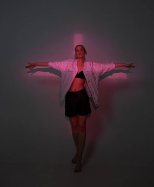 Havalı genç kız karanlık stüdyoda çapraz ışıkla dikiliyor.