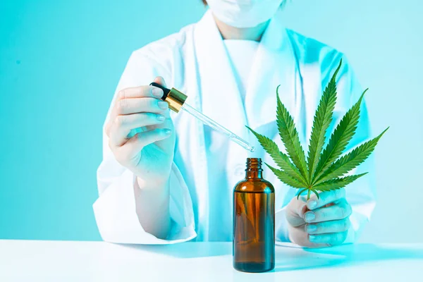 Gros plan du médecin avec une feuille de cannabis et une bouteille d'huile de cannabis développant des produits à base de chanvre en néon bleu — Photo