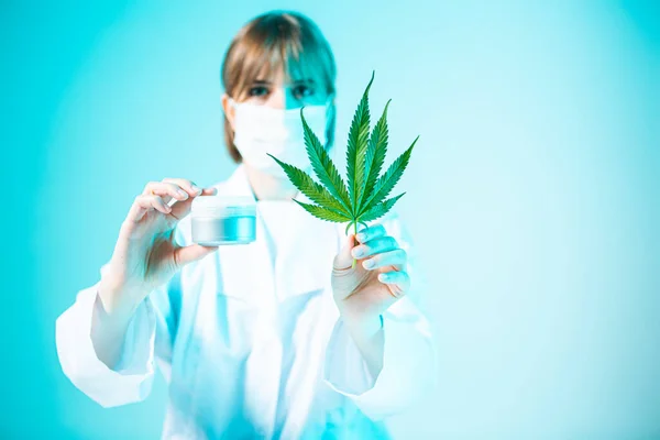Dermatologue scientifique féminine avec feuille de chanvre et crème naturelle à la lumière bleue néon, produits du cannabis pour soins de la peau — Photo
