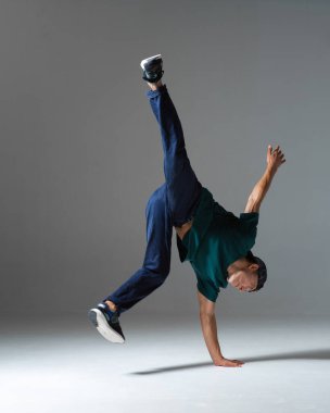 Gri arka planda tek başına duran havalı break dansçı adam dans ediyor. Breakdance dersleri