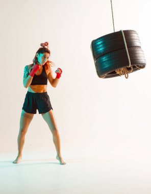 Neon ışıkta duran lastiklerden yapılmış kum torbasıyla atletik kadın eğitimi. Kadınların spor ve motivasyon konsepti