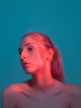 Yüzünde mercan ışığı ve çıplak omuzlarıyla genç ve güzel bir kızın stüdyo portresi.