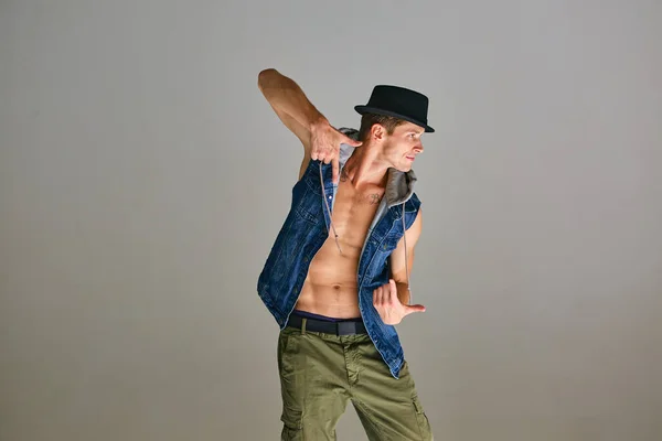 Młody facet breakdancer w kapeluszu taniec hip-hop w studio na szarym tle. Plakat szkoły tańca — Zdjęcie stockowe