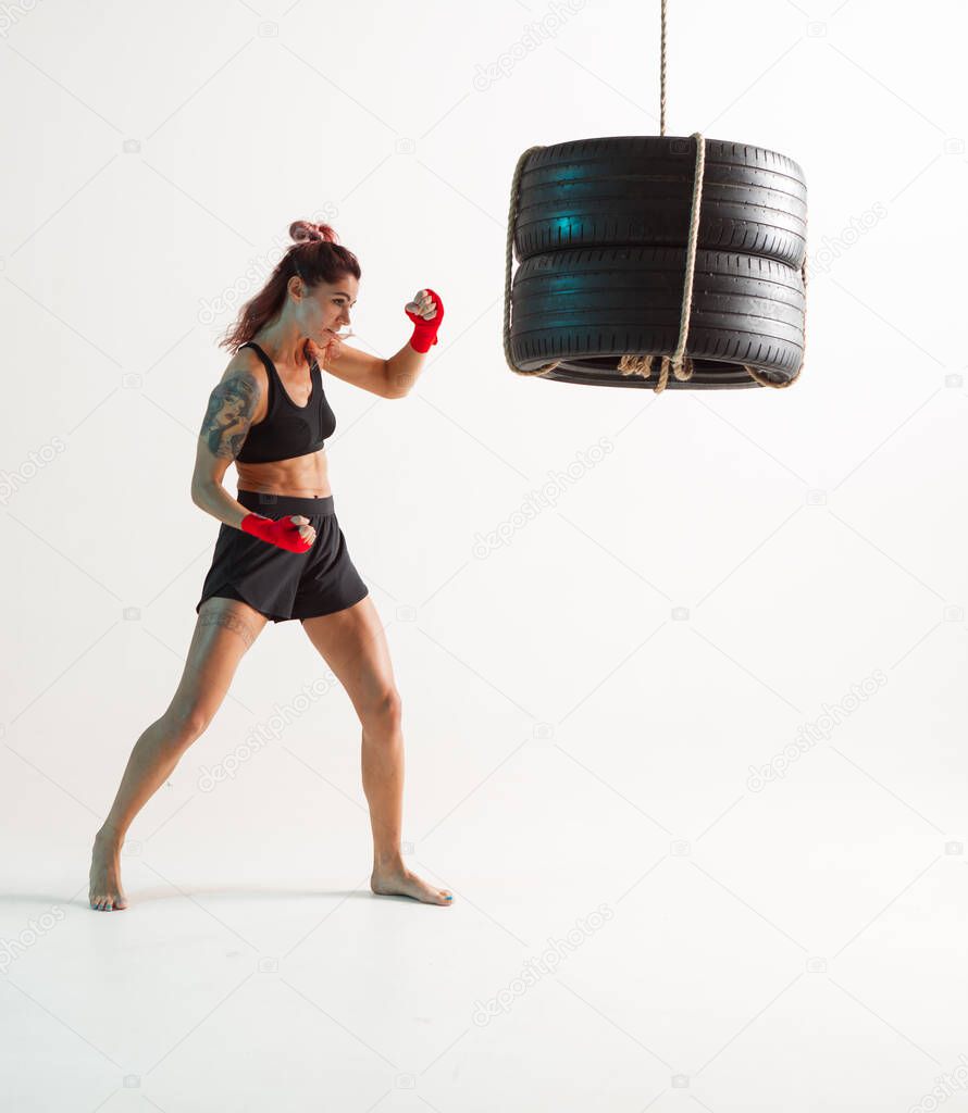 Athletic female fighter training with punching bag in studio. Womens sport, intensive workout