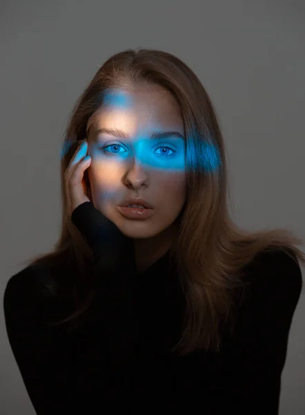 Stylová mladá dívka s modrým neonovým světlem na tváři, studiový portrét — Stock fotografie