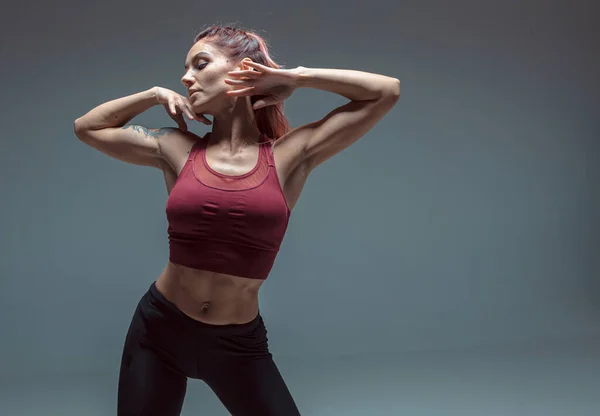 Portrait d'une jeune fille moderne exécutant des éléments de danse contemporaine sur un fond gris. — Photo