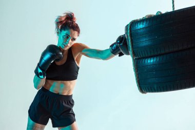 Boks eldivenli bir kadın dövüşçü eliyle lastiklere vuruyor.