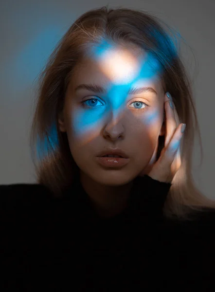 Portret van jong mooi meisje in donkere studio met blauw licht op haar gezicht — Stockfoto