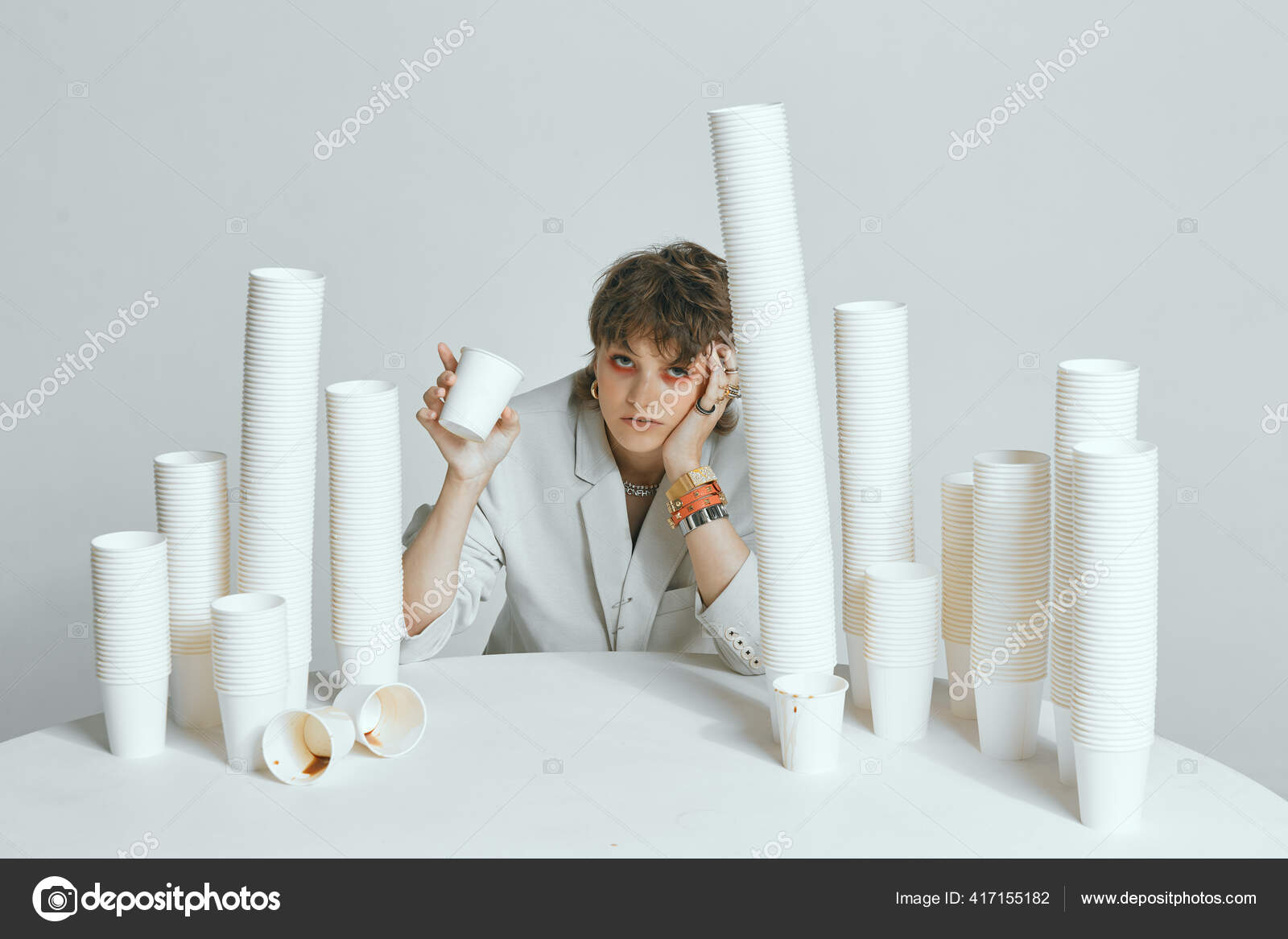 Tired female with lots of paper cups for coffee on gray studio ...