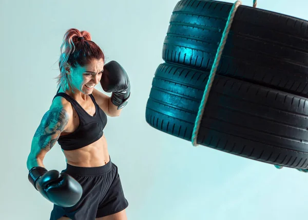 A female fighter in Boxing gloves strikes the tires with her hand — Stock Photo, Image