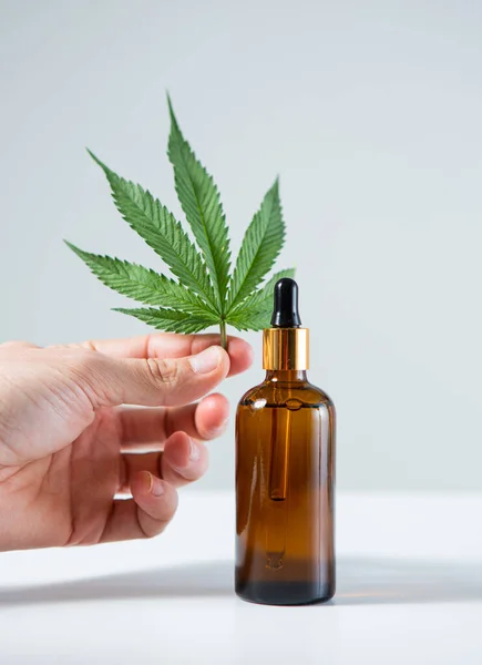 CBD血清大麻製品と灰色の背景に手に麻の葉でガラス瓶の閉鎖 — ストック写真