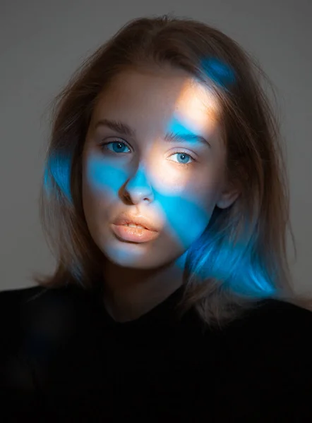 Stylová mladá dívka s modrým neonovým světlem na tváři, studiový portrét — Stock fotografie