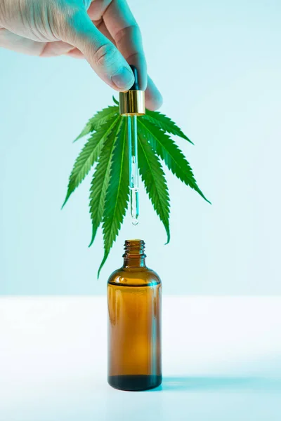 Hanfprodukt in Glasschablone, Cannabisblatt und Männerhand mit Pipette aus Cbd-Extrakt in Neonlicht — Stockfoto