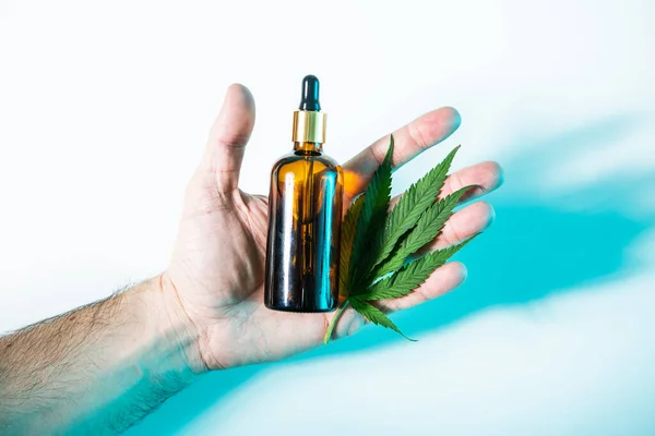 Hanf-Kosmetikprodukt in der Flasche und Cannabisblatt in der Hand im Neonlicht, Ansicht von oben — Stockfoto