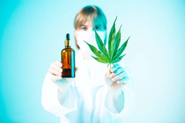 Jeune femme médecin avec pot en verre et feuille de chanvre dans les mains dans la lumière bleue néon. Médecine cannabis concept — Photo