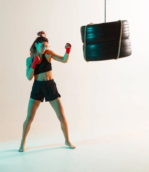 Lutador feminino desportivo boxe em saco de perfuração em luz de néon. Exercício de desporto feminino — Fotografia de Stock