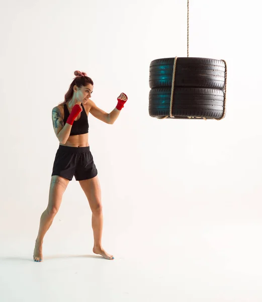 Αθλητική γυναικεία εκπαίδευση σε κομψά αθλητικά ρούχα με σάκο του μποξ στο στούντιο. Γυναικεία αθλήματα καταπολέμηση προπόνηση — Φωτογραφία Αρχείου
