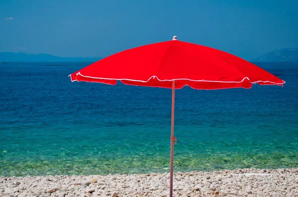 Plaj çakıl taşları ve bir yaz gününde kırmızı şemsiye — Stok fotoğraf