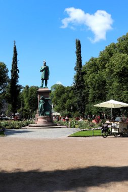 Finlandiya 'nın Helsinki kentindeki Esplanadi Parkı' nda sıcak bir yaz gününde Johan Runeberg 'in yiyecek satan bir el arabasının yanındaki heykeline giden bir yol görülüyordu.. 
