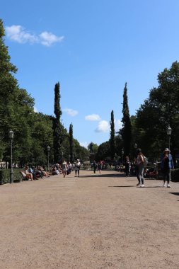 İnsanlar sıcak bir yaz gününde Finlandiya 'nın Helsinki şehrinde parkta yürürler ve otururlar.. 