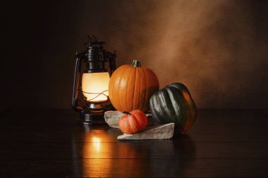 Light shining on a llantern next to pumpkins and squash on a wood table. 