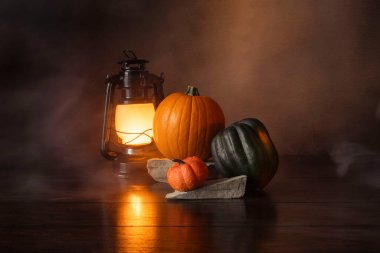 Balkabaklarının ve meşe palamudu kabağının yanındaki ahşap bir masada yanan bir fenerin etrafında hafif bir duman..