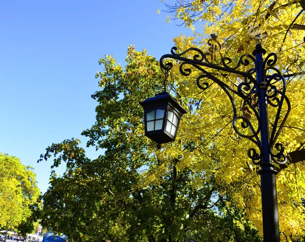 in a city park stands a tall decorative lantern against a background of yellow leaves of trees