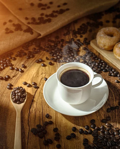 Kahve fincanı ve kavrulmuş kahve çekirdekleri. yumuşak güneş ışığı ile ahşap arka plan üzerinde 
