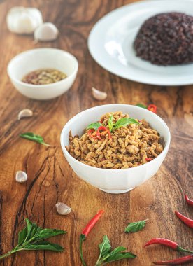 Bir tabak ve biber balık sosu, ahşap bir masaya yerleştirilen bir tabakta kıyılmış domuz eti ve berry pirinç ile kızarmış fesleğen karıştırın