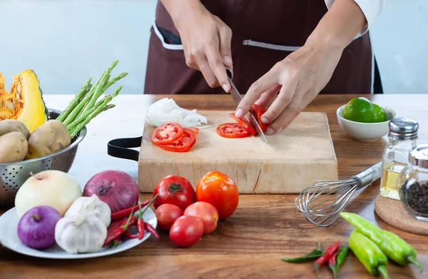 Nahaufnahme. Die Hand des Kochs schneidet Gemüse. auf einem hölzernen Schneidebrett mit einem Messer auf dem mit Gemüse gefüllten Küchentisch — Stockfoto